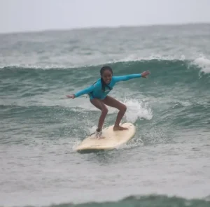 A young girl balances on her surfboard, mastering the waves of Tofo Beach as part of a beginner's surf lesson with Wutsita Surf School in Mozambique.