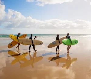 A group of surfers walking along Praia do Tofo, their boards in hand, ready for an exciting surf session organized by Wutsita Surf School & Rentals in Tofo, Mozambique.
